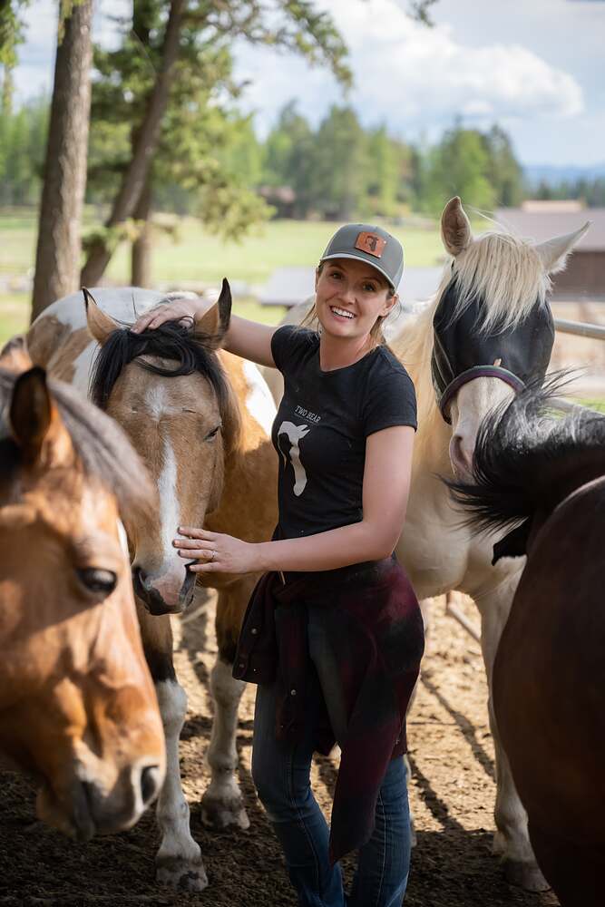 Kat with one hand on a horse's face and three more horses crowded in around her
