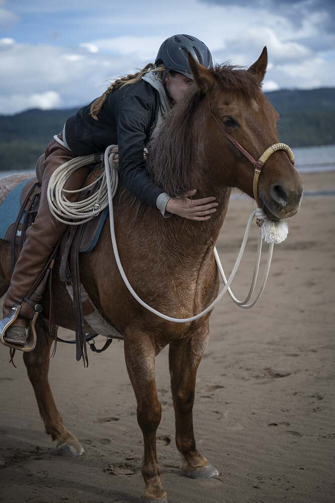 Kat leaning right down in the saddle with both arms around her horse's neck
