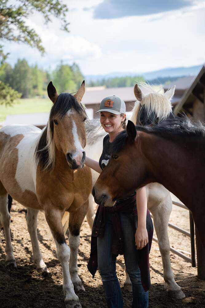 Kat standing between a paint and a buckskin in the corral, a hand on each