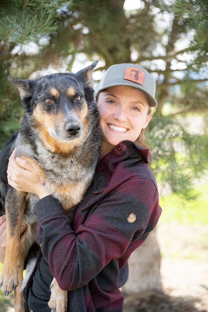Kat with her blue heeler gathered up in both arms, the dog looking straight at the camera