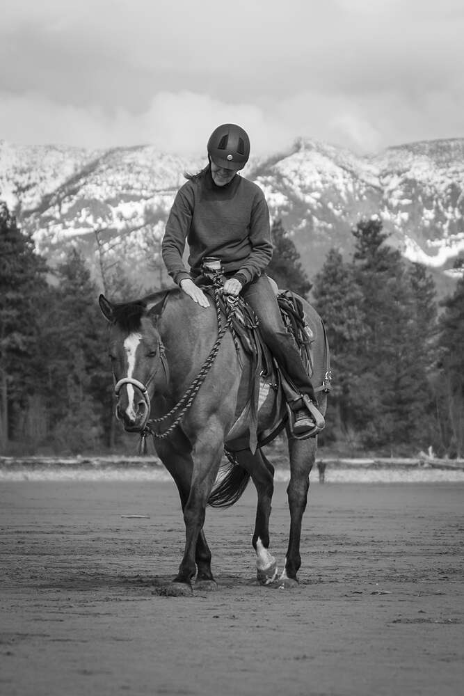 A rider on a grey horse coming up the sand with the mountains behind, in black and white