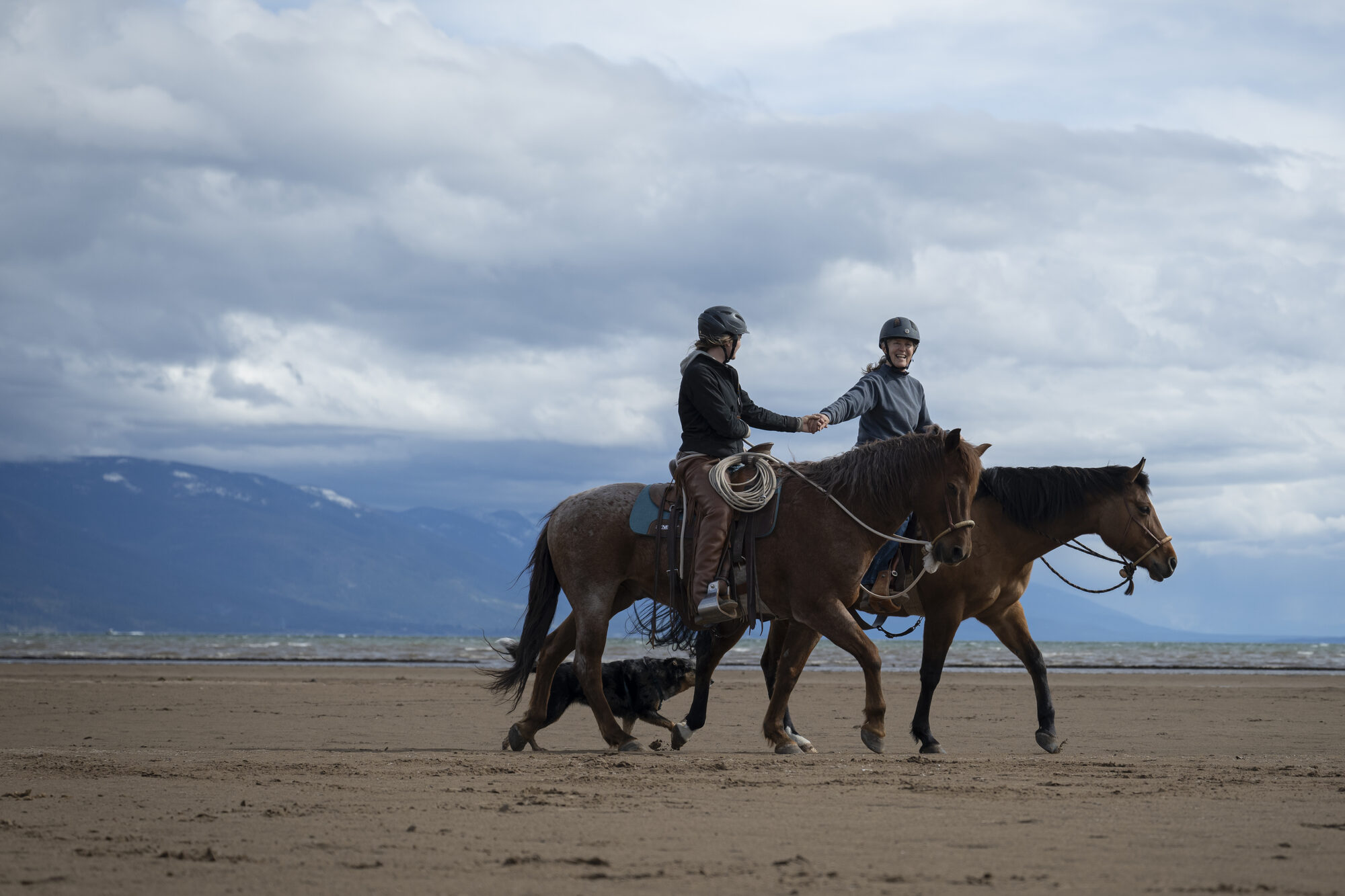 Kat riding with her mother and their dog along the flats at Somers, Flathead Lake and the mountains behind them